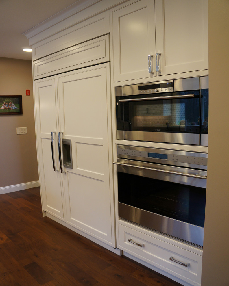 Example of a large l-shaped medium tone wood floor enclosed kitchen design in Boston with white cabinets, white backsplash, stainless steel appliances, an island, recessed-panel cabinets, granite countertops and subway tile backsplash