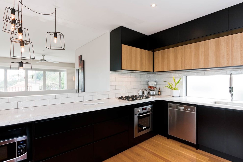 Photo of a mid-sized contemporary u-shaped eat-in kitchen in Sydney with a single-bowl sink, flat-panel cabinets, black cabinets, marble benchtops, window splashback, stainless steel appliances, medium hardwood floors, no island, white splashback, brown floor and white benchtop.