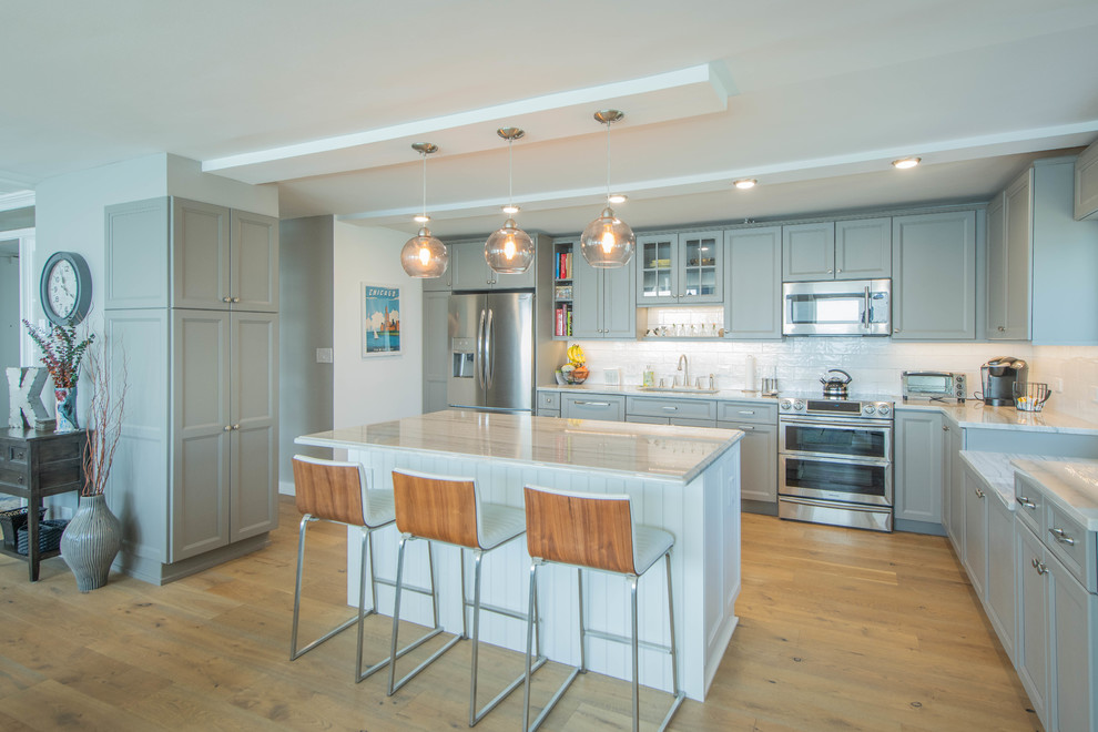 Design ideas for a transitional u-shaped kitchen in Chicago with an undermount sink, recessed-panel cabinets, grey cabinets, white splashback, stainless steel appliances, medium hardwood floors, with island, brown floor and white benchtop.