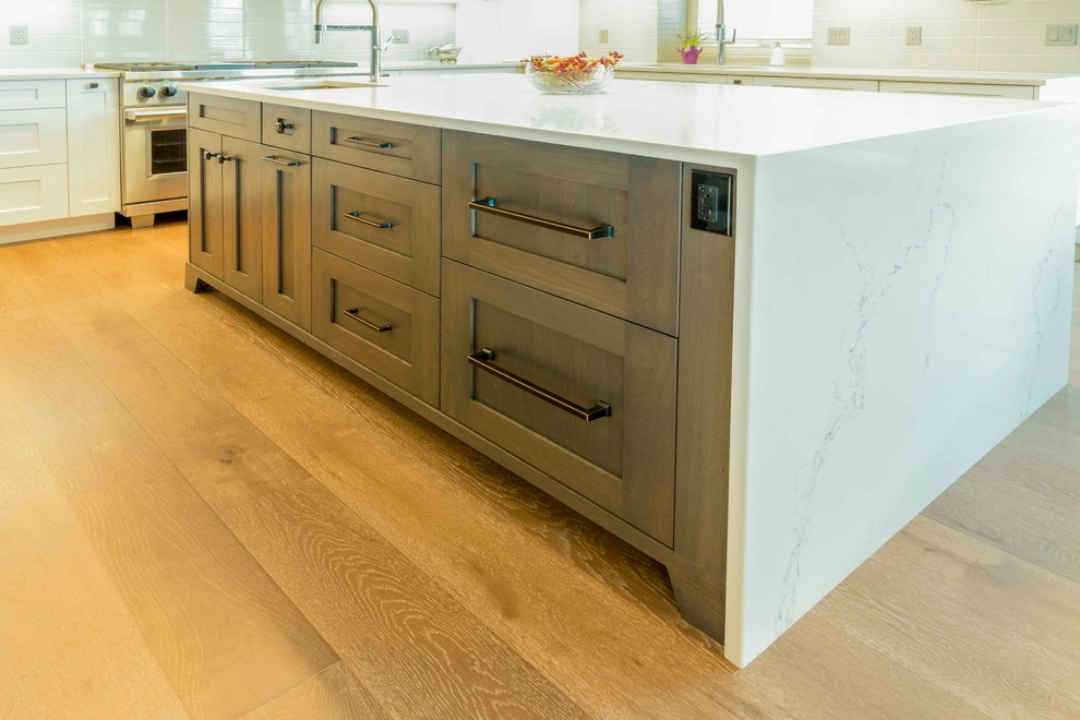 Example of a mid-sized transitional u-shaped medium tone wood floor and brown floor kitchen design in Calgary with an undermount sink, flat-panel cabinets, white cabinets, marble countertops, gray backsplash, ceramic backsplash, paneled appliances and an island