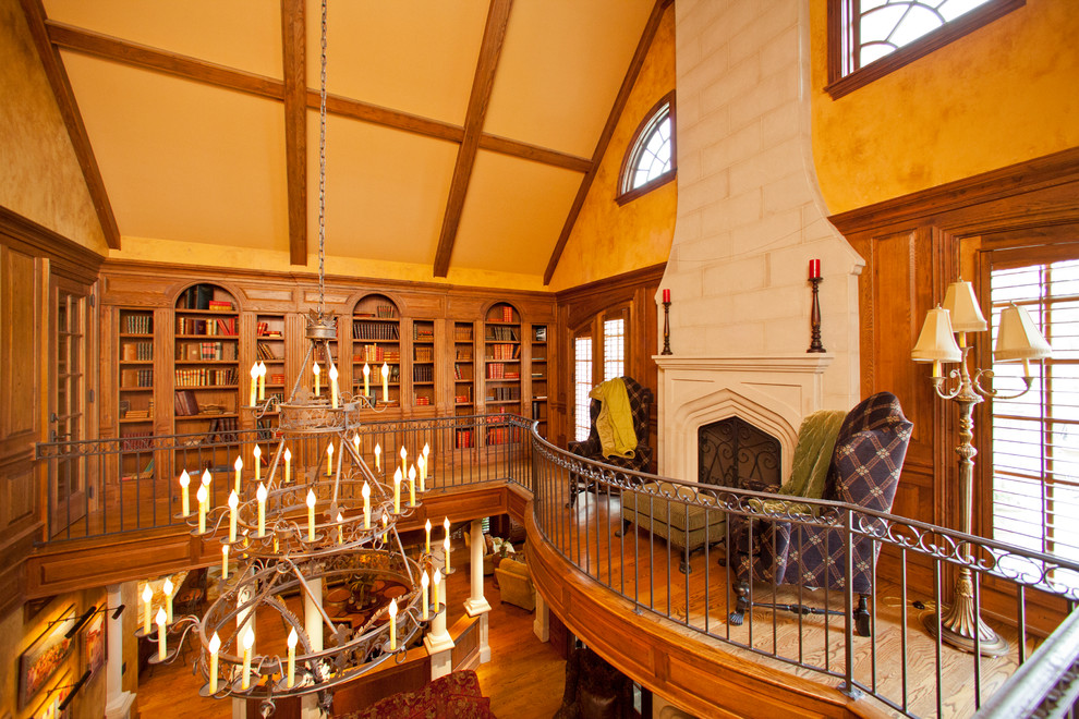 Inspiration for a mid-sized traditional loft-style living room in Raleigh with a library, yellow walls, medium hardwood floors, a standard fireplace, a wood fireplace surround and no tv.