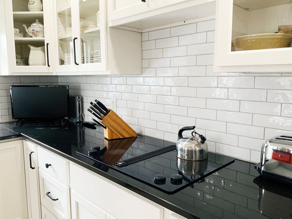 Inspiration for a large country l-shaped eat-in kitchen in Indianapolis with a double-bowl sink, glass-front cabinets, white cabinets, granite benchtops, white splashback, subway tile splashback, stainless steel appliances, with island, white floor and black benchtop.