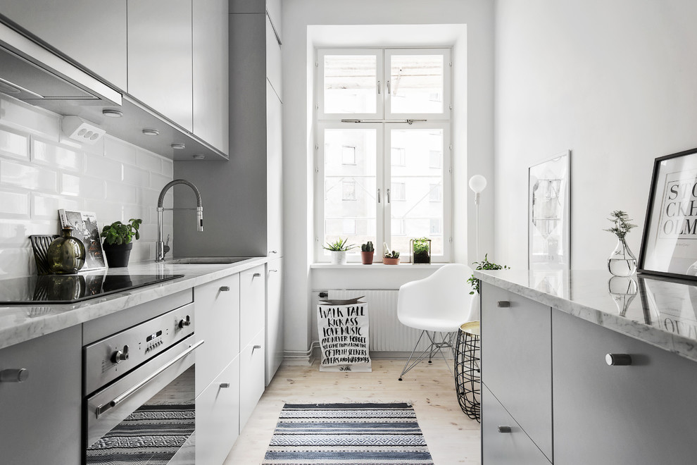 This is an example of a mid-sized scandinavian galley separate kitchen in Stockholm with an undermount sink, flat-panel cabinets, grey cabinets, white splashback, subway tile splashback, light hardwood floors, marble benchtops, stainless steel appliances and no island.