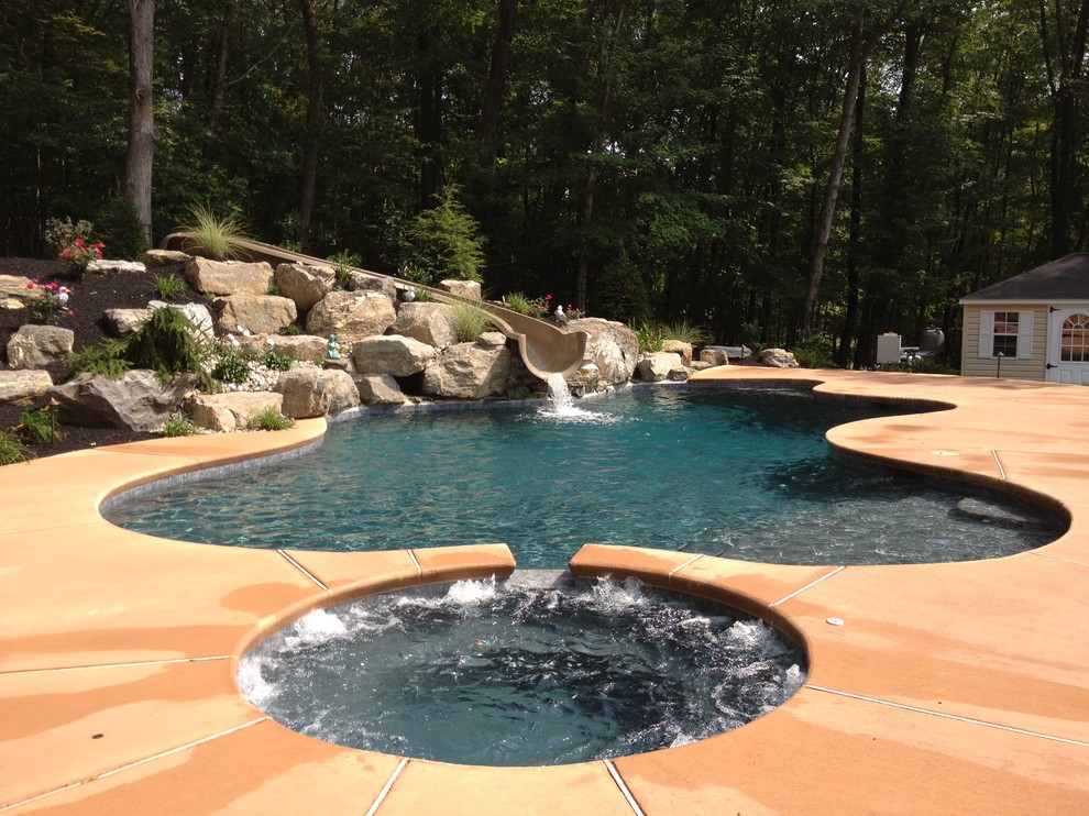 This is an example of a traditional backyard custom-shaped natural pool in Philadelphia with decking and a hot tub.