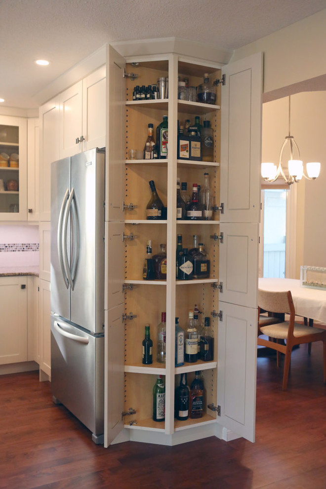Example of a mid-sized transitional l-shaped medium tone wood floor and brown floor open concept kitchen design in Calgary with an undermount sink, shaker cabinets, white cabinets, granite countertops, white backsplash, mosaic tile backsplash, stainless steel appliances, an island and beige countertops