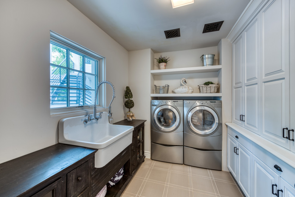 This is an example of a country u-shaped dedicated laundry room in Phoenix with a farmhouse sink, raised-panel cabinets, white cabinets, wood benchtops, white walls, a side-by-side washer and dryer, beige floor and brown benchtop.