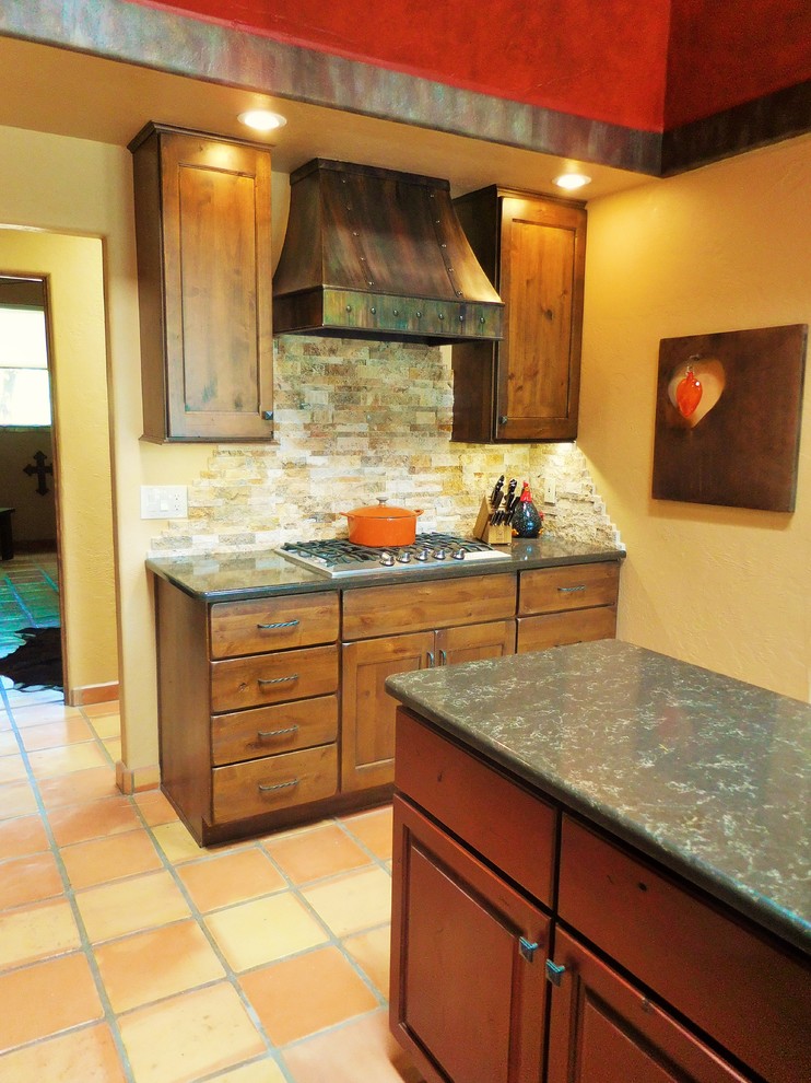 Example of a small southwest terra-cotta tile enclosed kitchen design in Phoenix with a farmhouse sink, shaker cabinets, brown cabinets, quartz countertops, beige backsplash, stone tile backsplash, stainless steel appliances and an island