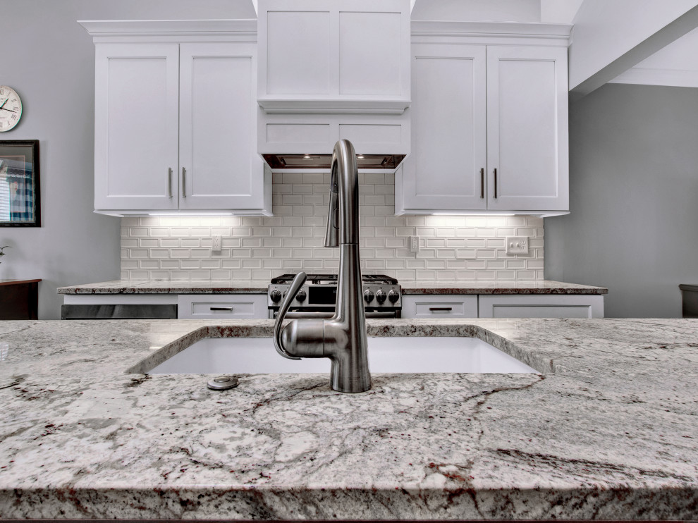 Eat-in kitchen - mid-sized transitional medium tone wood floor, brown floor and vaulted ceiling eat-in kitchen idea in St Louis with an undermount sink, shaker cabinets, white cabinets, granite countertops, white backsplash, subway tile backsplash, stainless steel appliances, an island and multicolored countertops