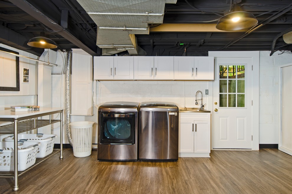 Inspiration for a mid-sized industrial utility room in DC Metro with an integrated sink, shaker cabinets, white cabinets, white walls, laminate floors, a side-by-side washer and dryer and brown floor.