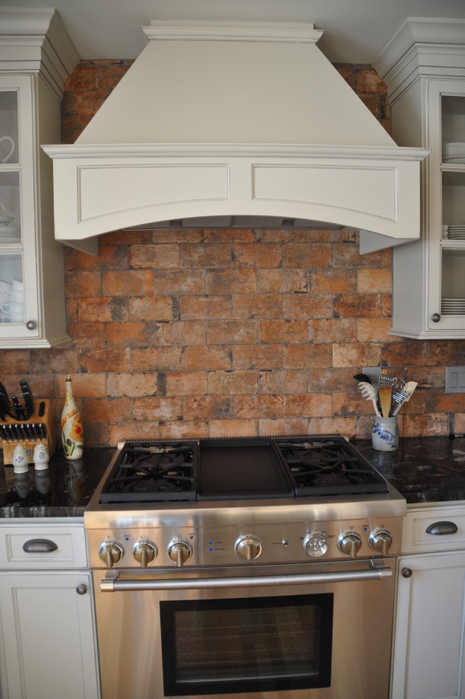 Mid-sized mountain style u-shaped medium tone wood floor eat-in kitchen photo in Baltimore with a farmhouse sink, recessed-panel cabinets, white cabinets, granite countertops, red backsplash, stone tile backsplash, stainless steel appliances and an island