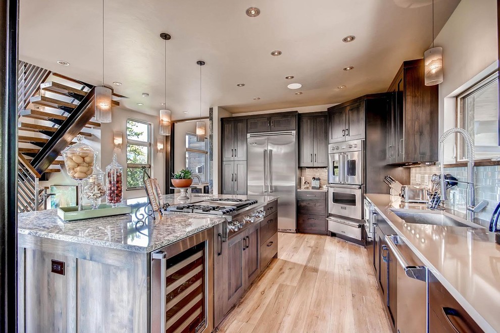 Large mountain style l-shaped light wood floor and brown floor open concept kitchen photo in Denver with an undermount sink, shaker cabinets, dark wood cabinets, quartz countertops, gray backsplash, subway tile backsplash, stainless steel appliances and an island