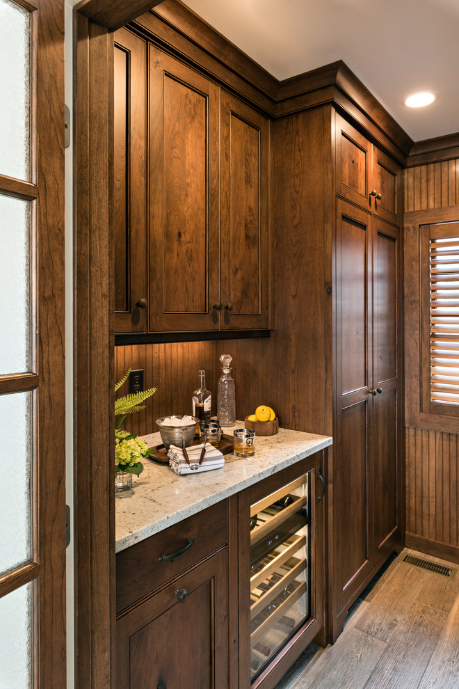 This is an example of a mid-sized country galley wet bar in Boston with beaded inset cabinets, dark wood cabinets, granite benchtops, brown splashback, timber splashback, medium hardwood floors, brown floor and white benchtop.