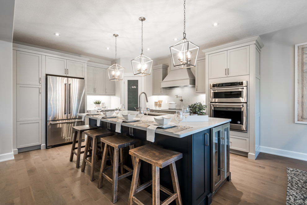Example of a transitional u-shaped medium tone wood floor and brown floor eat-in kitchen design in Toronto with a farmhouse sink, shaker cabinets, white cabinets, white backsplash, stainless steel appliances, an island and white countertops