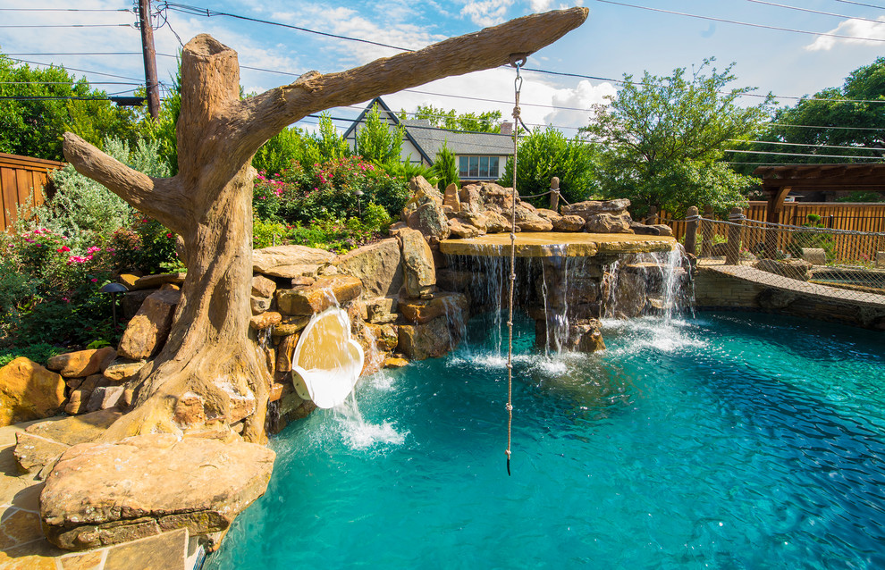 This is an example of a large tropical backyard custom-shaped pool in Dallas with a water slide and natural stone pavers.
