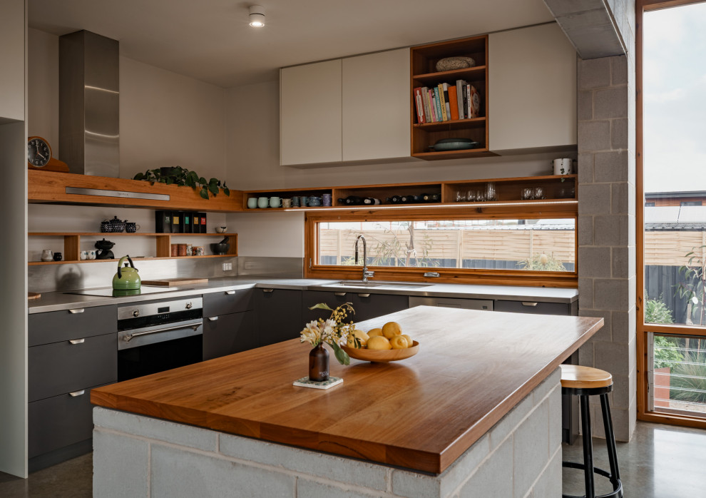 Photo of a mid-sized midcentury l-shaped eat-in kitchen in Geelong with a double-bowl sink, grey cabinets, stainless steel benchtops, white splashback, black appliances, concrete floors, with island, grey floor, brown benchtop and coffered.