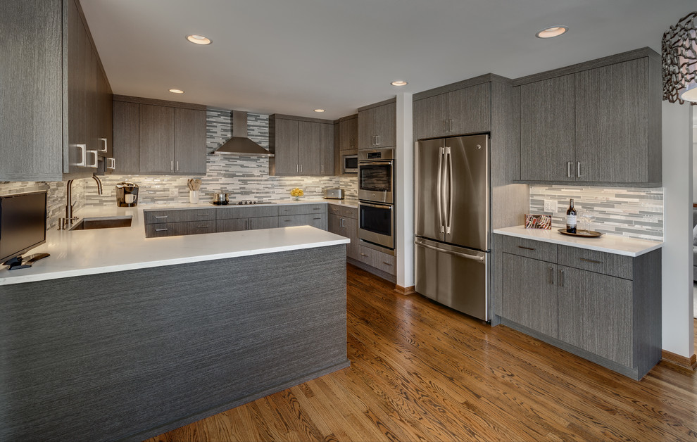 Mid-sized contemporary u-shaped eat-in kitchen in Chicago with a single-bowl sink, flat-panel cabinets, grey cabinets, quartz benchtops, multi-coloured splashback, glass tile splashback, stainless steel appliances, medium hardwood floors, a peninsula and brown floor.