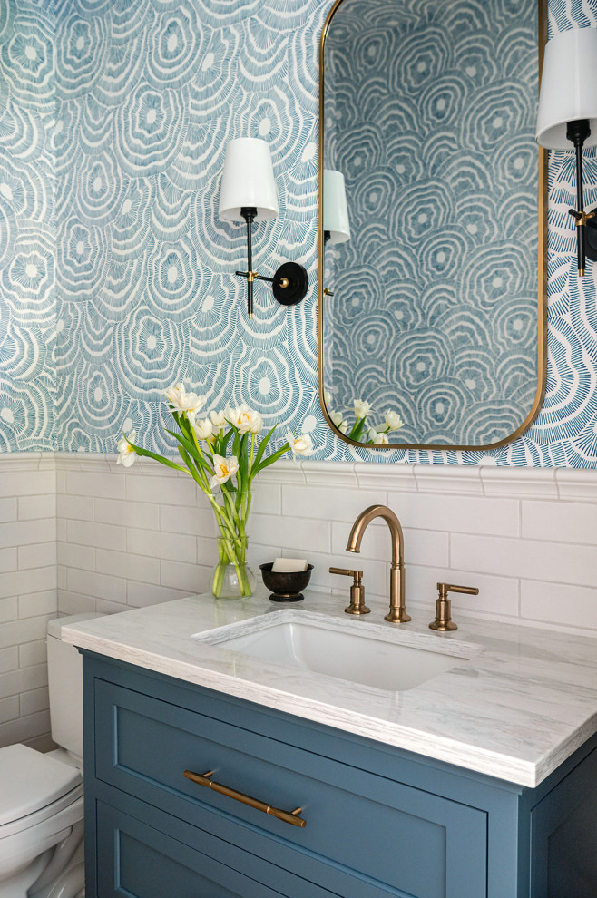 Powder room - small coastal white tile and subway tile wallpaper powder room idea in Grand Rapids with shaker cabinets, blue cabinets, a two-piece toilet, blue walls, an undermount sink, marble countertops, white countertops and a freestanding vanity