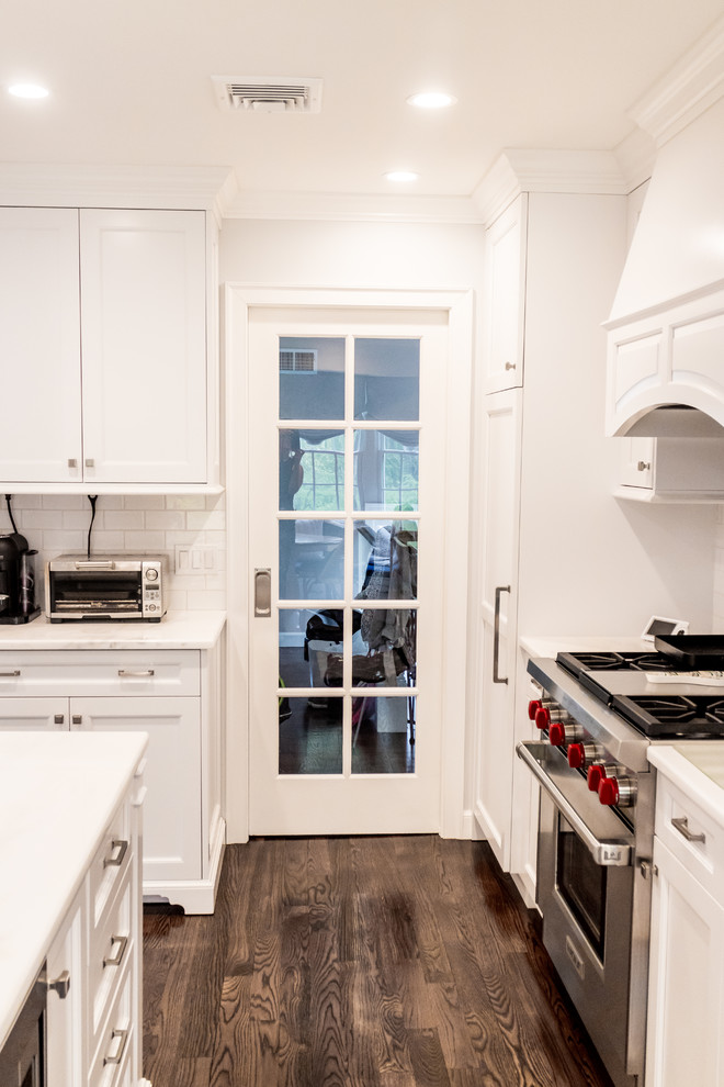 Inspiration for a mid-sized transitional dark wood floor and brown floor enclosed kitchen remodel in New York with a farmhouse sink, recessed-panel cabinets, white cabinets, quartzite countertops, white backsplash, subway tile backsplash, stainless steel appliances and an island