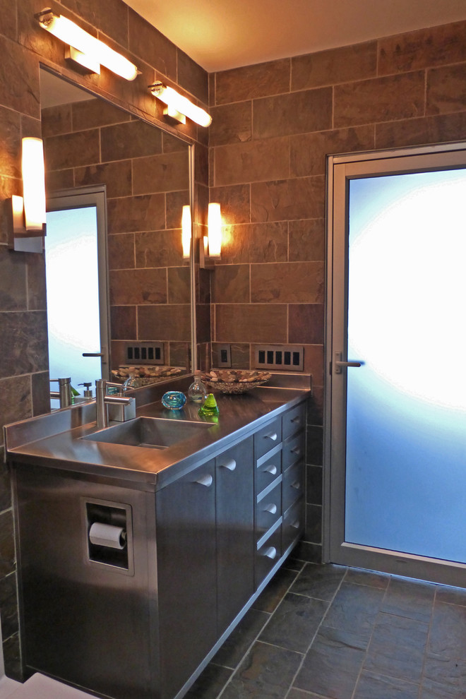 This is an example of a small midcentury master bathroom in Cincinnati with an integrated sink, flat-panel cabinets, grey cabinets, stainless steel benchtops, an alcove tub, a shower/bathtub combo, a one-piece toilet, gray tile, stone tile, green walls and slate floors.