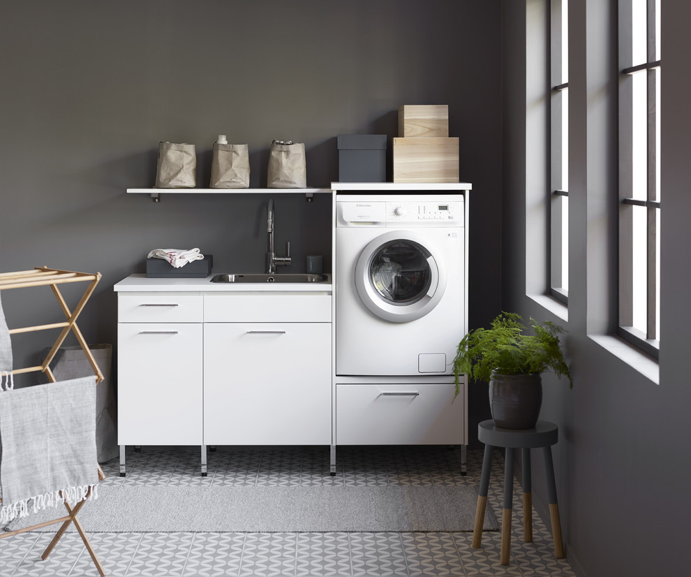 Photo of a mid-sized scandinavian single-wall utility room in Gothenburg with a single-bowl sink, flat-panel cabinets, white cabinets, grey walls, porcelain floors and grey floor.