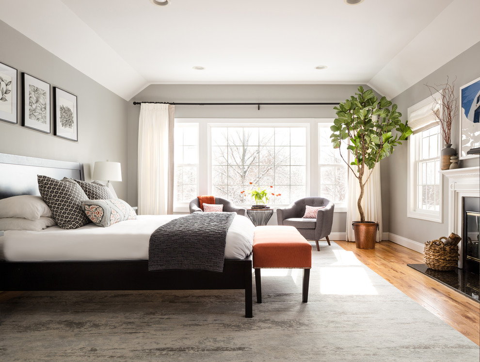 Large transitional master bedroom in New York with grey walls, medium hardwood floors, a standard fireplace, a stone fireplace surround and brown floor.