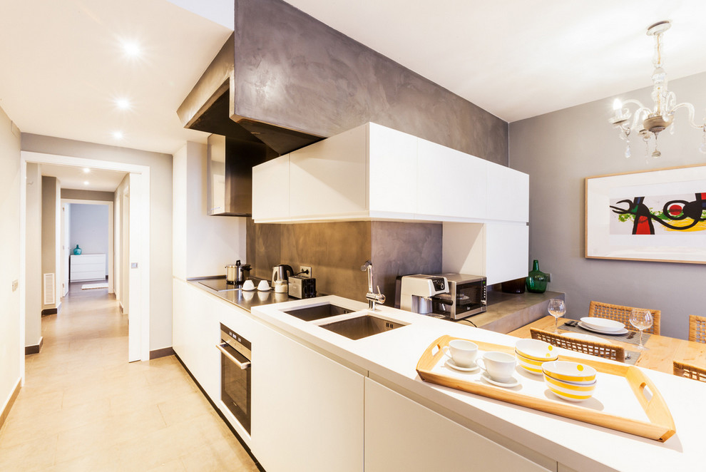 This is an example of a mid-sized contemporary single-wall eat-in kitchen in Barcelona with a double-bowl sink, white cabinets, solid surface benchtops, grey splashback, cement tile splashback, stainless steel appliances, porcelain floors, a peninsula and flat-panel cabinets.