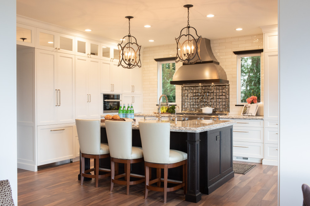 Inspiration for a large transitional l-shaped eat-in kitchen in Seattle with a farmhouse sink, white cabinets, granite benchtops, metallic splashback, glass tile splashback, stainless steel appliances, dark hardwood floors, with island, brown floor, multi-coloured benchtop and shaker cabinets.