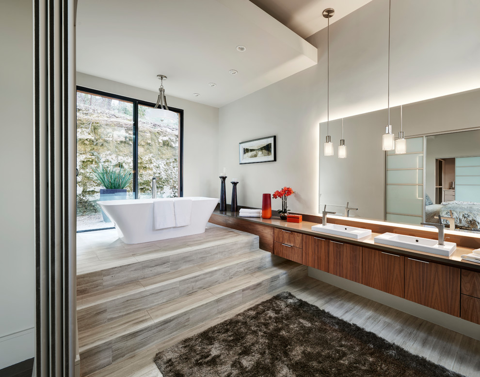 This is an example of a large contemporary master bathroom in Austin with flat-panel cabinets, medium wood cabinets, a freestanding tub, a curbless shower, a two-piece toilet, gray tile, ceramic tile, white walls, ceramic floors, a vessel sink, quartzite benchtops and grey floor.