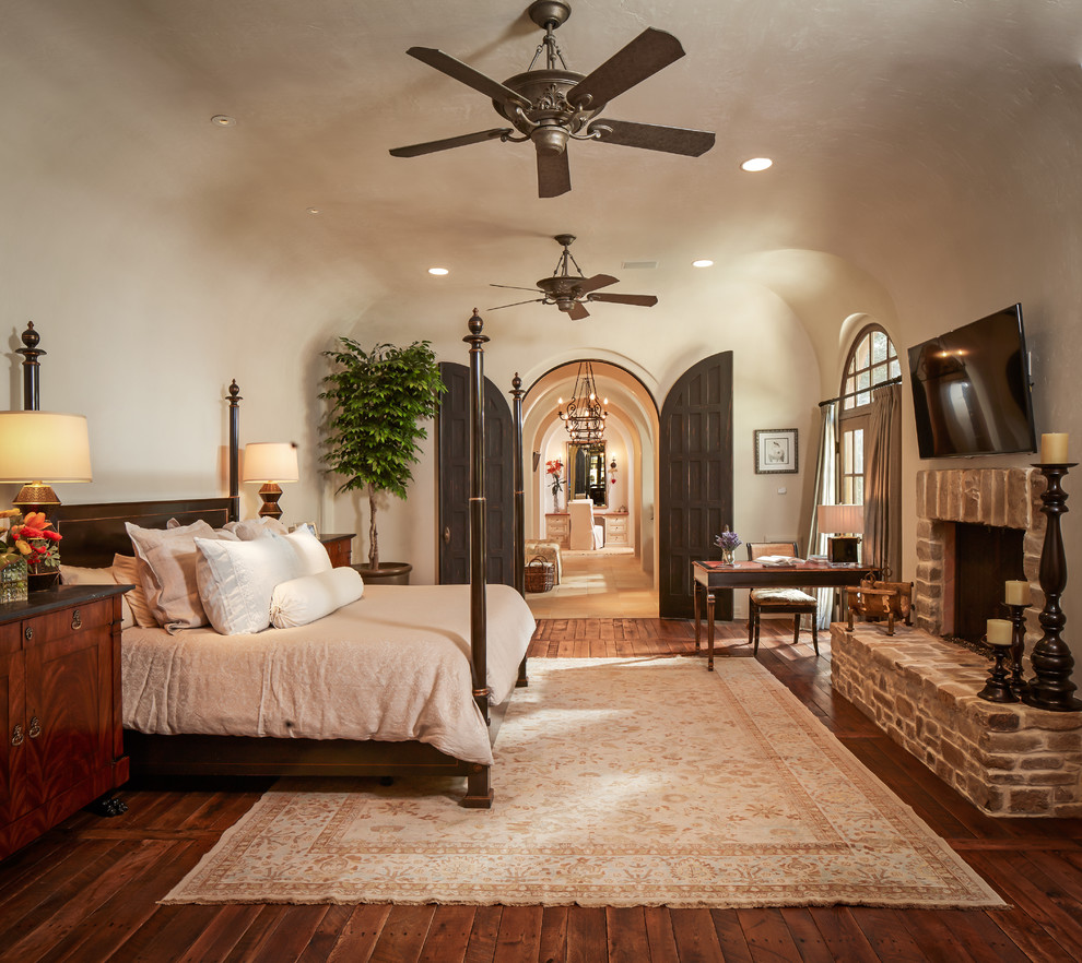 Photo of a mid-sized mediterranean master bedroom in Houston with beige walls, a standard fireplace, a brick fireplace surround, dark hardwood floors and brown floor.