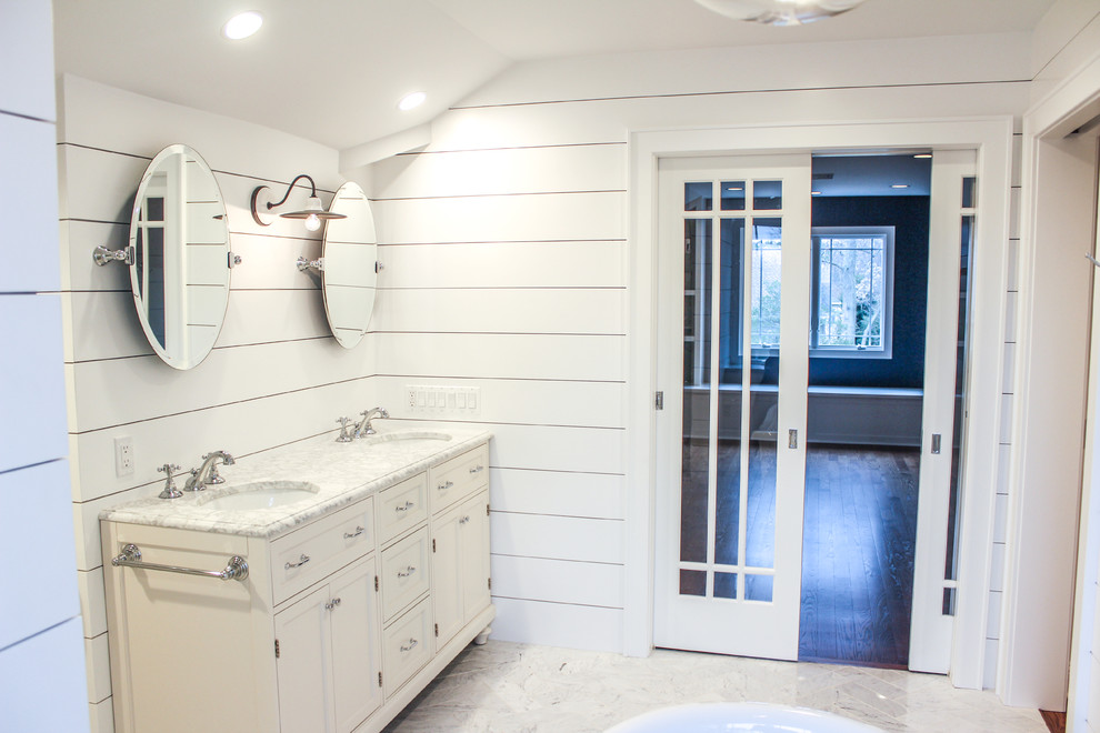 This is an example of a large arts and crafts master bathroom in New York with furniture-like cabinets, white cabinets, a freestanding tub, an alcove shower, a one-piece toilet, white tile, ceramic tile, white walls, ceramic floors, a drop-in sink and marble benchtops.