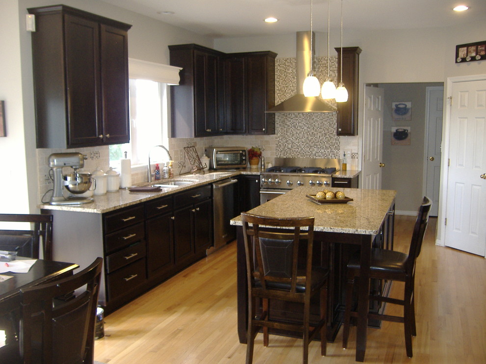 Inspiration for a mid-sized transitional l-shaped light wood floor eat-in kitchen remodel in Indianapolis with an undermount sink, flat-panel cabinets, dark wood cabinets, granite countertops, stainless steel appliances, beige backsplash, stone tile backsplash and an island