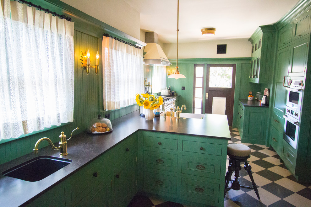 This is an example of a large arts and crafts l-shaped separate kitchen in Los Angeles with a farmhouse sink, shaker cabinets, green cabinets, quartz benchtops, green splashback, white appliances, limestone floors and a peninsula.