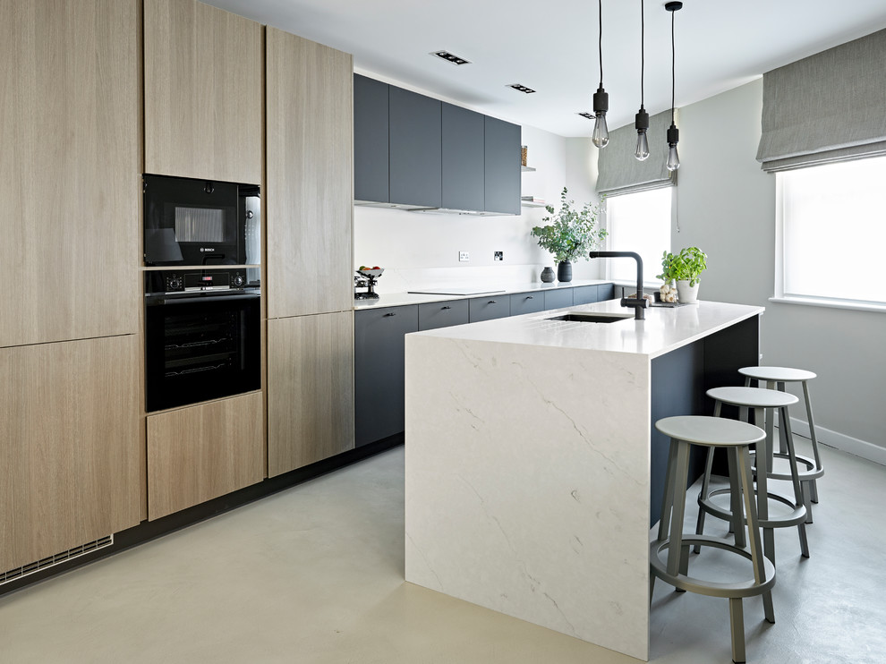 Photo of a small contemporary kitchen in London with an undermount sink, flat-panel cabinets, marble benchtops, black appliances, with island, grey floor, white benchtop, black cabinets and concrete floors.