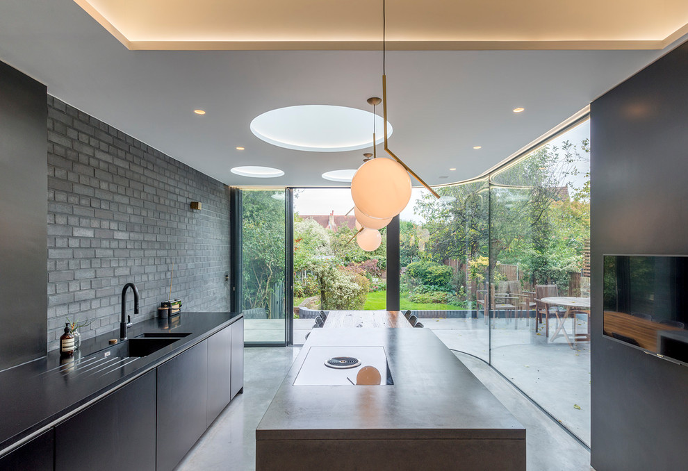 Inspiration for a mid-sized modern galley eat-in kitchen in London with an integrated sink, flat-panel cabinets, black cabinets, solid surface benchtops, brick splashback, black appliances, concrete floors, with island and grey floor.