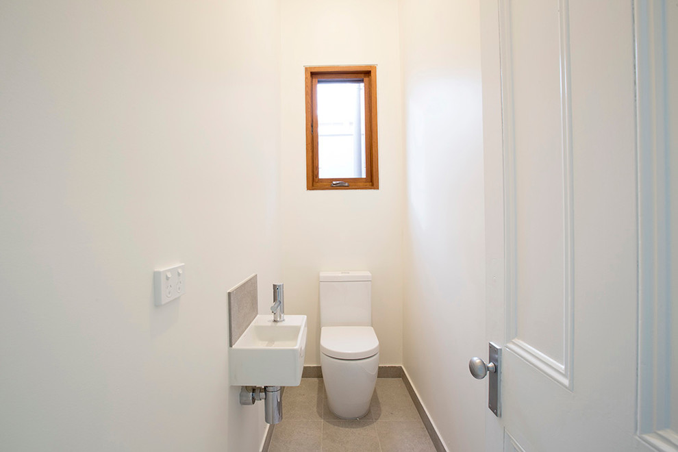 Photo of a small contemporary powder room in Melbourne with a two-piece toilet, white walls, ceramic floors, a wall-mount sink and beige floor.