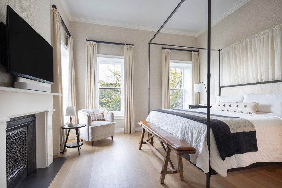 Klassisches Hauptschlafzimmer mit beiger Wandfarbe, hellem Holzboden, Kamin, Kaminumrandung aus Stein und braunem Boden in New York