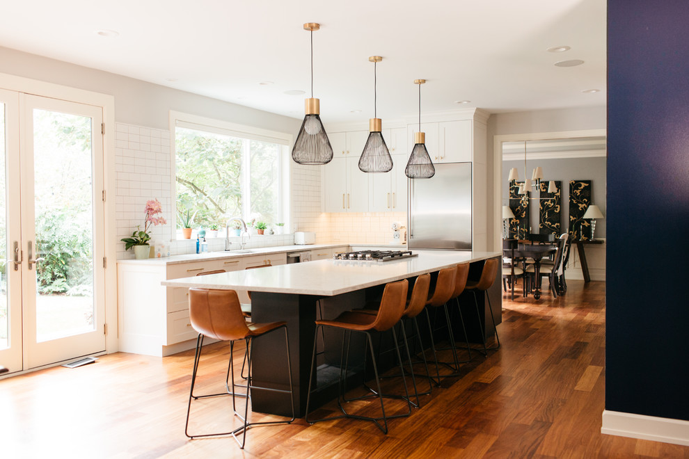Design ideas for a large transitional u-shaped open plan kitchen in Seattle with shaker cabinets, white cabinets, quartz benchtops, with island, white benchtop, an undermount sink, white splashback, subway tile splashback, stainless steel appliances, medium hardwood floors and brown floor.