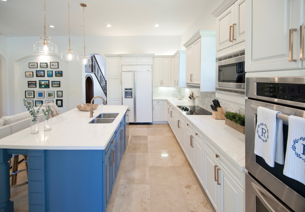 This is an example of a large nautical galley kitchen in Miami with a submerged sink, raised-panel cabinets, white cabinets, engineered stone countertops, grey splashback, stone tiled splashback, integrated appliances, travertine flooring, an island, beige floors and white worktops.