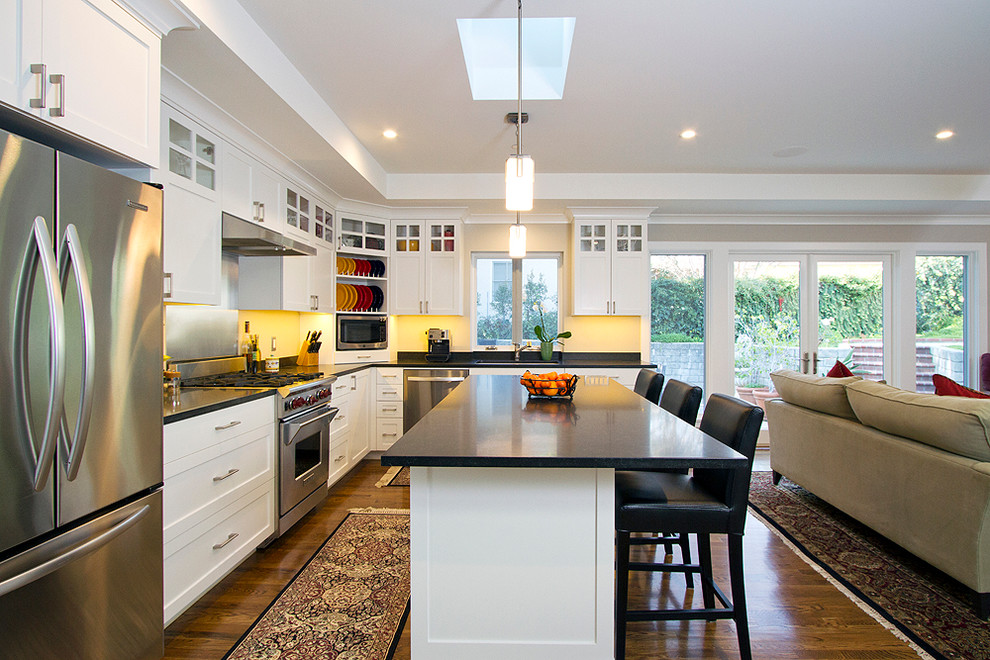 Photo of a transitional kitchen in Los Angeles with an undermount sink, shaker cabinets, white cabinets, granite benchtops, stainless steel appliances, medium hardwood floors, with island and black benchtop.