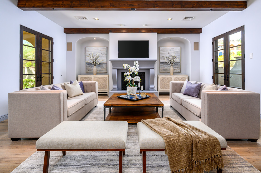 Modelo de sala de estar abierta tradicional renovada grande con paredes grises, suelo de madera clara, todas las chimeneas, marco de chimenea de hormigón, televisor colgado en la pared y vigas vistas