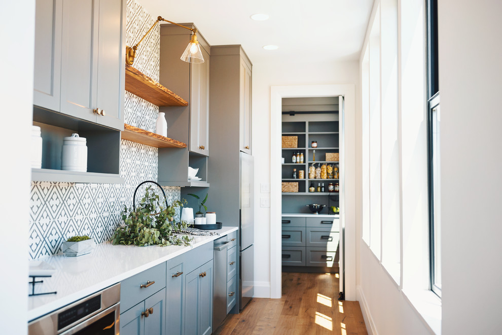 Inspiration for a country single-wall kitchen in Seattle with recessed-panel cabinets, grey cabinets, multi-coloured splashback, cement tile splashback, stainless steel appliances, medium hardwood floors, no island, brown floor and white benchtop.