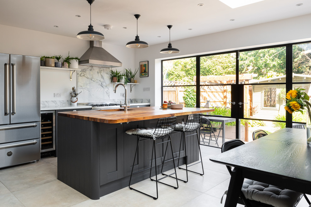 Photo of a modern kitchen in London with black cabinets, wood worktops, white splashback, marble splashback, a breakfast bar and grey floors.