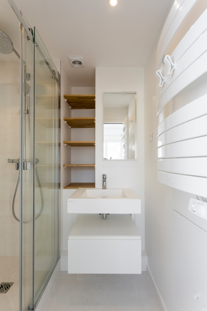 Inspiration for a mid-sized modern master bathroom in Paris with a curbless shower, white walls, white floor, a sliding shower screen, flat-panel cabinets, white cabinets, a two-piece toilet, beige tile, limestone, ceramic floors, a wall-mount sink, solid surface benchtops and white benchtops.