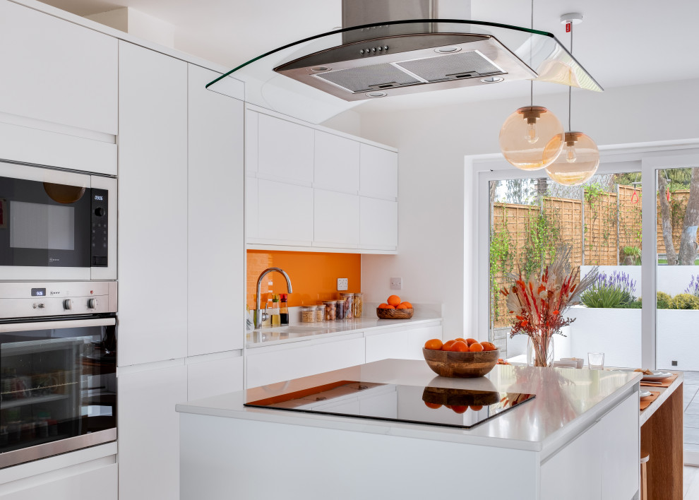 Mid-sized contemporary galley open plan kitchen in Gloucestershire with an integrated sink, white cabinets, quartz benchtops, orange splashback, panelled appliances, porcelain floors, beige floor, white benchtop, flat-panel cabinets, glass sheet splashback and with island.