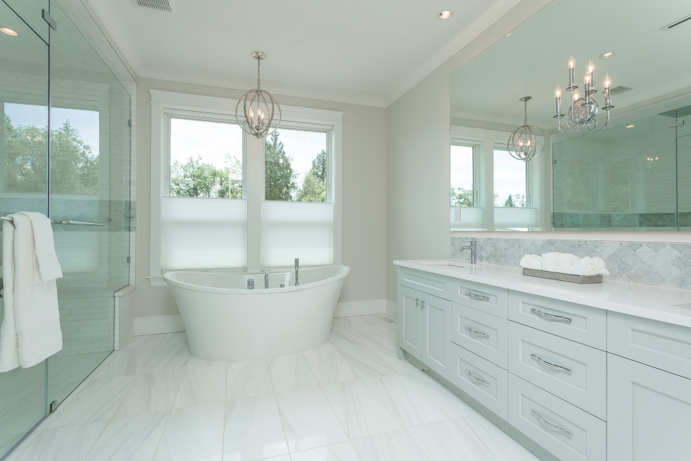 Photo of a large traditional master bathroom in Vancouver with shaker cabinets, white cabinets, a freestanding tub, a curbless shower, gray tile, marble, beige walls, ceramic floors, an undermount sink, solid surface benchtops, white floor, a hinged shower door, white benchtops, a shower seat, a double vanity and a built-in vanity.