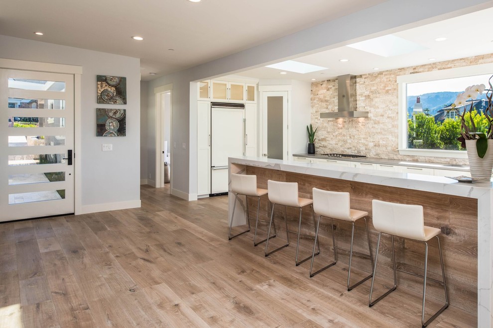 Inspiration for a large transitional u-shaped light wood floor open concept kitchen remodel in Orange County with shaker cabinets, white cabinets, stone tile backsplash, no island, an undermount sink, beige backsplash, stainless steel appliances and gray countertops