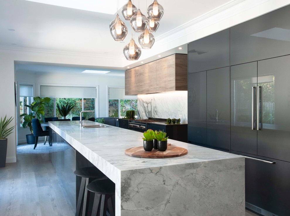 Design ideas for a large contemporary galley open plan kitchen in Sydney with a drop-in sink, marble benchtops, stone slab splashback, black appliances, with island, flat-panel cabinets, brown cabinets, grey splashback, medium hardwood floors, grey floor and grey benchtop.