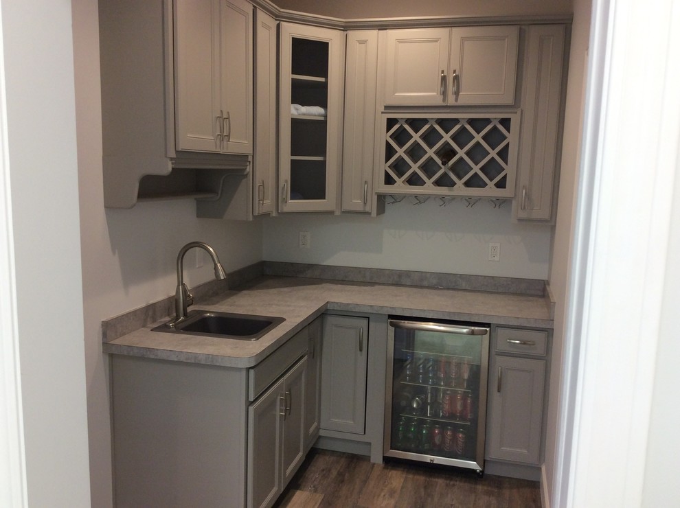 This is an example of a traditional galley home bar in Grand Rapids with a drop-in sink, grey cabinets, laminate benchtops, dark hardwood floors and recessed-panel cabinets.