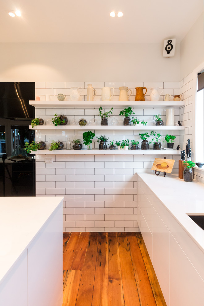 Photo of a mid-sized contemporary l-shaped eat-in kitchen in Auckland with an undermount sink, quartz benchtops, yellow splashback, subway tile splashback, black appliances, medium hardwood floors and with island.