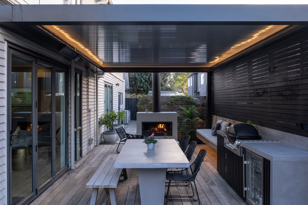 Contemporary backyard and ground level deck in Auckland with with fireplace and a pergola.